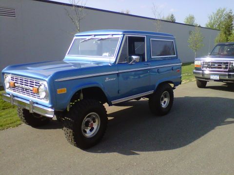 1995 Ford Bronco - A classic blue Ford Bronco is parked next to another Ford vehicle.