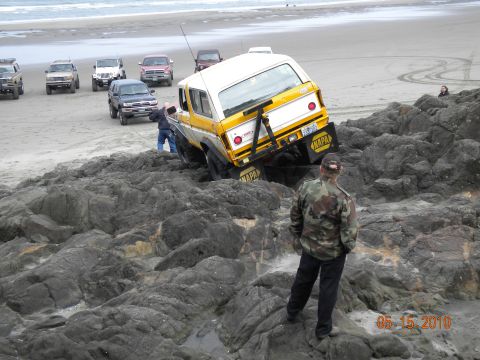 1994 Ford Explorer - A group of off-road vehicles are seen on a beach, with one vehicle stuck on a rocky outcrop near the water's edge.