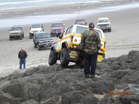 1994 Ford Explorer - Several off-road vehicles are gathered on a sandy and rocky beach near the ocean.