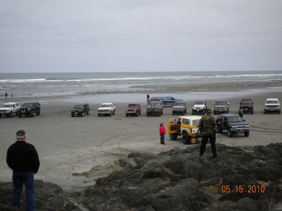 Beach scene with multiple SUVs and trucks parked on the sand near the ocean
