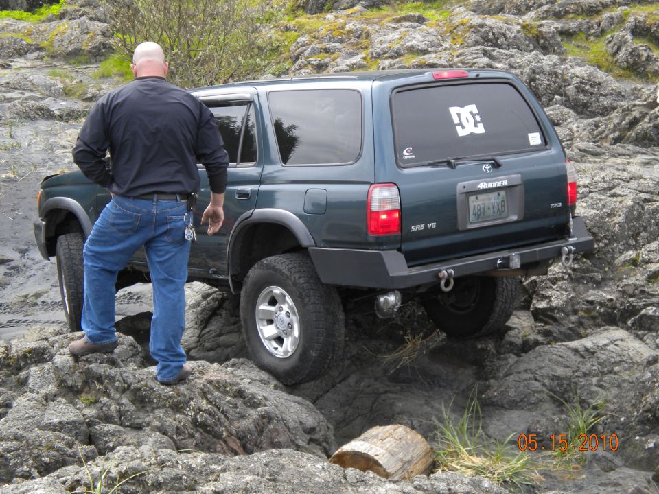 Man standing next to a dark green Toyota 4Runner on a rocky trail. The 4Runner has a custom bumper and a DC Shoes sticker on the rear window