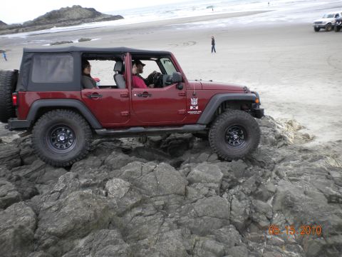 1994 Ford Explorer - A red Jeep Wrangler navigates rocky terrain near the ocean, with another vehicle visible on the sandy beach.