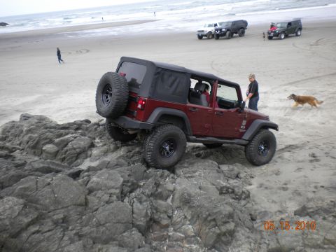 1994 Ford Explorer - Several vehicles are on the beach near the ocean, with one Jeep Wrangler navigating rocky terrain.