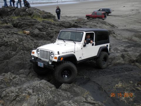 1994 Ford Explorer - White Jeep Wrangler Rubicon navigates rocky coastal terrain with other vehicles in the distance.