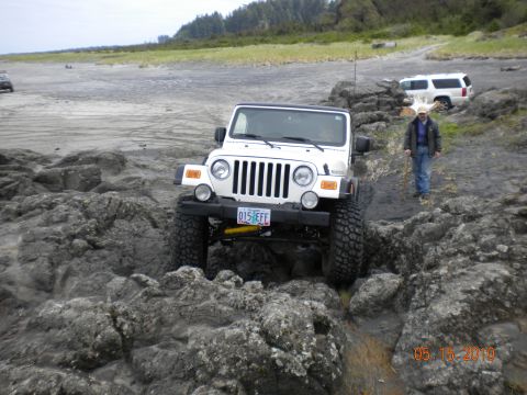 1994 Ford Explorer - A white Jeep Wrangler navigates a rocky beach path, with another SUV parked further back on the sand.