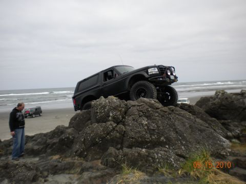 1994 Ford Explorer - A black SUV is positioned on rocks near a beach, with another vehicle visible in the distance.
