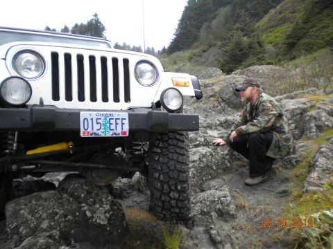 1994 Ford Explorer - A man in camouflage crouches near a white Jeep Wrangler on a rocky, off-road path.
