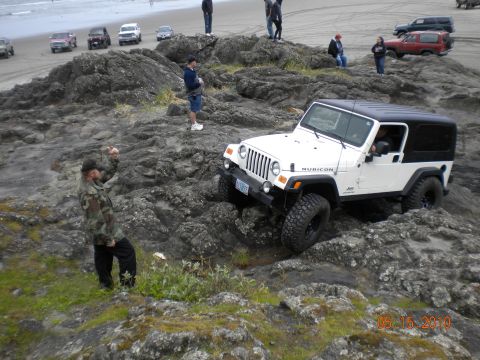 1994 Ford Explorer - A white Jeep Wrangler Rubicon is driven over rocks on a beach, with other vehicles visible in the background.
