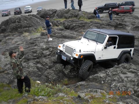1994 Ford Explorer - A white Jeep Wrangler Rubicon is driven over rocks near the beach, with several other vehicles visible in the distance.