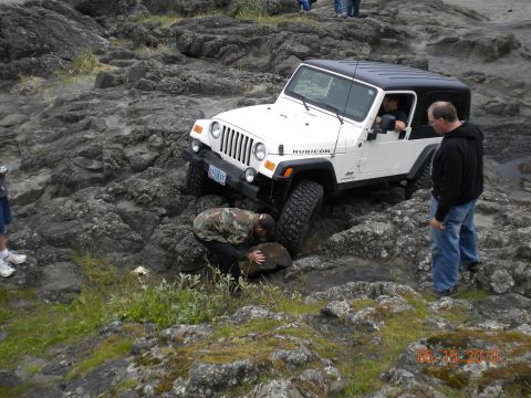 1994 Ford Explorer - A white Jeep Wrangler Rubicon is being carefully driven over a rocky, uneven surface, with onlookers observing the maneuver.