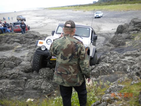 1994 Ford Explorer - A person stands near an SUV on a rocky shoreline, with water visible in the background.