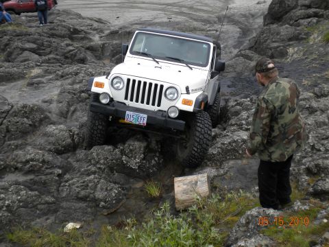 1994 Ford Explorer - A white Jeep Wrangler Rubicon is driven over a rocky obstacle course, with a person in camouflage watching.
