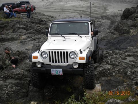 1994 Ford Explorer - A white Jeep Wrangler Rubicon navigates a rocky trail, with other vehicles visible in the background.