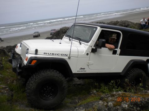 1994 Ford Explorer - A white Jeep Wrangler Rubicon is parked on a rocky shore with the ocean in the background.