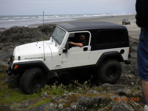 1994 Ford Explorer - A white Jeep Wrangler Rubicon is parked on rocks near the ocean with another vehicle in the background on the beach.