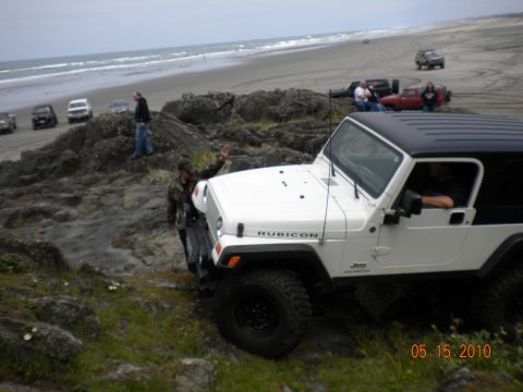 1994 Ford Explorer - A white Jeep Wrangler Rubicon navigates rocky terrain on a beach, with other vehicles visible in the background.