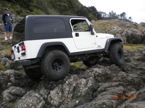 1994 Ford Explorer - A white Jeep Wrangler Rubicon navigates a rocky coastal path, with a person standing on a hill in the background.