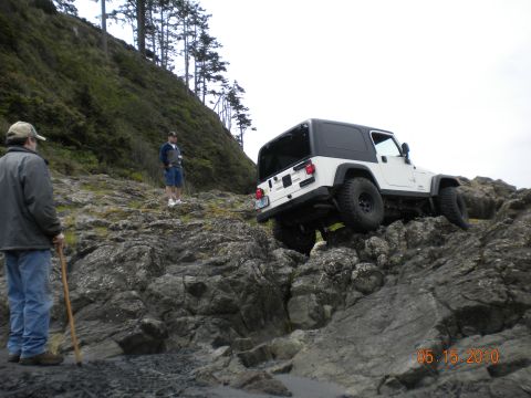 1994 Ford Explorer - White Jeep Wrangler TJ navigating a rocky coastal trail with two observers present.