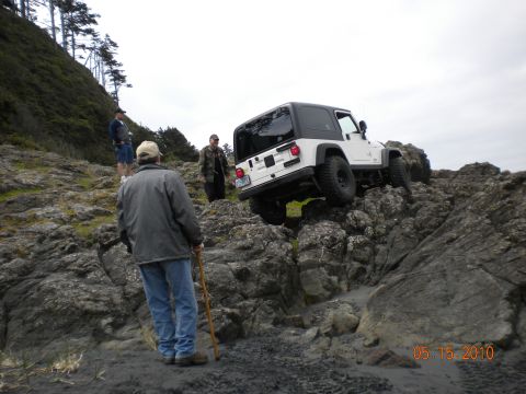 1994 Ford Explorer - A white Jeep Wrangler navigates a rocky coastal path, with onlookers observing the off-road excursion.