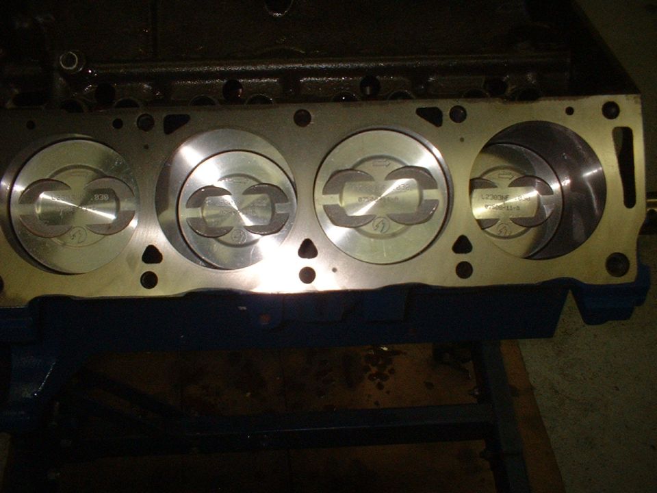 Engine block with four pistons visible, some with part numbers