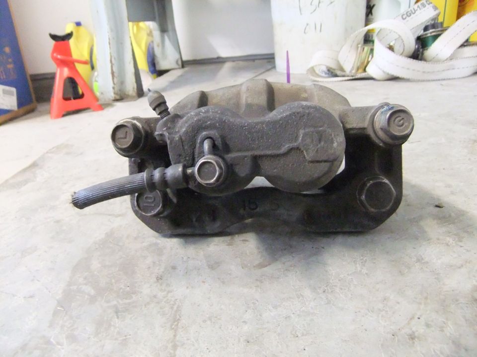 Car brake caliper with a ribbed hose attached. Some numbers are visible on the caliper body