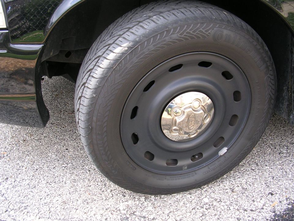 Black Ford Crown Victoria wheel with a chrome hubcap showing the Ford logo, Continental tire, and black steel rim
