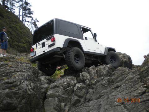 1994 Ford Explorer - A white Jeep Wrangler TJ navigates a rocky terrain, with a person standing on the left side of the frame.