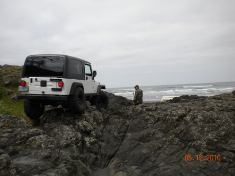 1994 Ford Explorer - Jeep Wrangler parked on rocks by the ocean on a cloudy day.