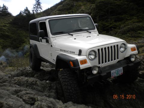 1994 Ford Explorer - A white Jeep Wrangler Rubicon is shown on a rocky terrain with trees and smoke in the distance.