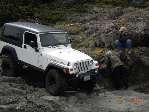 1994 Ford Explorer - A white Jeep Wrangler Rubicon navigates a rocky coastal path, with two individuals observing the off-road adventure.