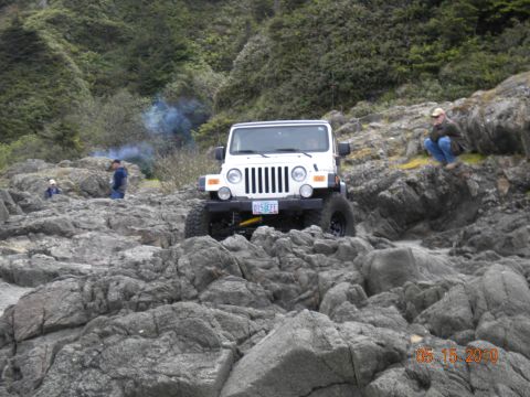 1994 Ford Explorer - A white Jeep Wrangler navigates a rocky coastal terrain, with onlookers observing the off-road activity.