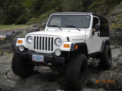 1994 Ford Explorer - A white Jeep Wrangler Rubicon is parked on a rocky shore with trees in the background.