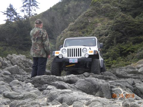 1994 Ford Explorer - A person in camouflage stands on a rocky shore next to a white Jeep Wrangler.