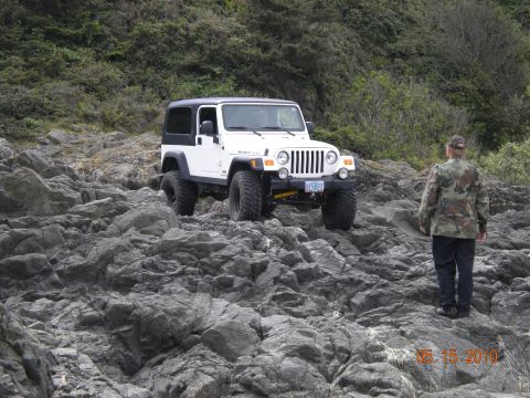 1994 Ford Explorer - A white Jeep Wrangler navigates a rocky coastal path, with a person observing the scene.