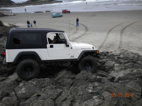 1994 Ford Explorer - Jeep Wrangler Rubicon navigating rocky terrain near the ocean, with other vehicles on the beach.