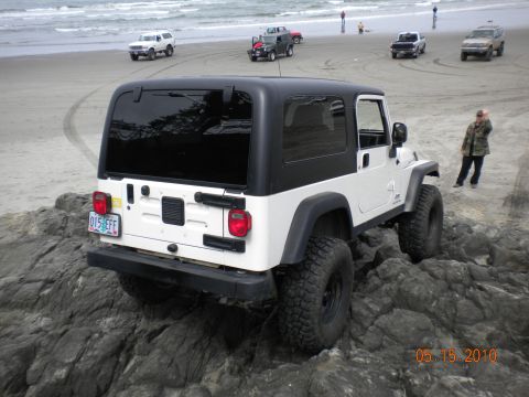1994 Ford Explorer - A white Jeep Wrangler is parked on rocks near the ocean, with other vehicles visible on the beach.