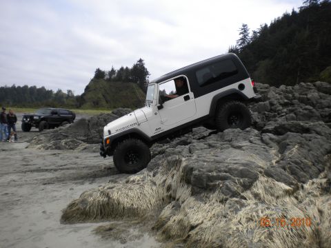 1994 Ford Explorer - A white Jeep Wrangler Rubicon navigates a rocky coastal terrain with another SUV in the background.