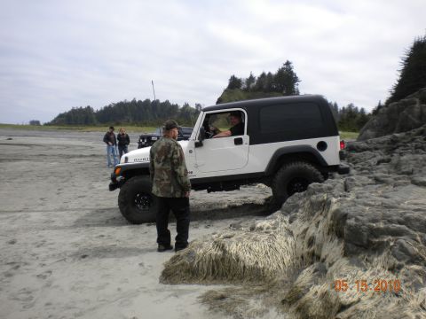 1994 Ford Explorer - A white Jeep Wrangler Rubicon is driven over rocks on a beach, with other vehicles and people in the background.