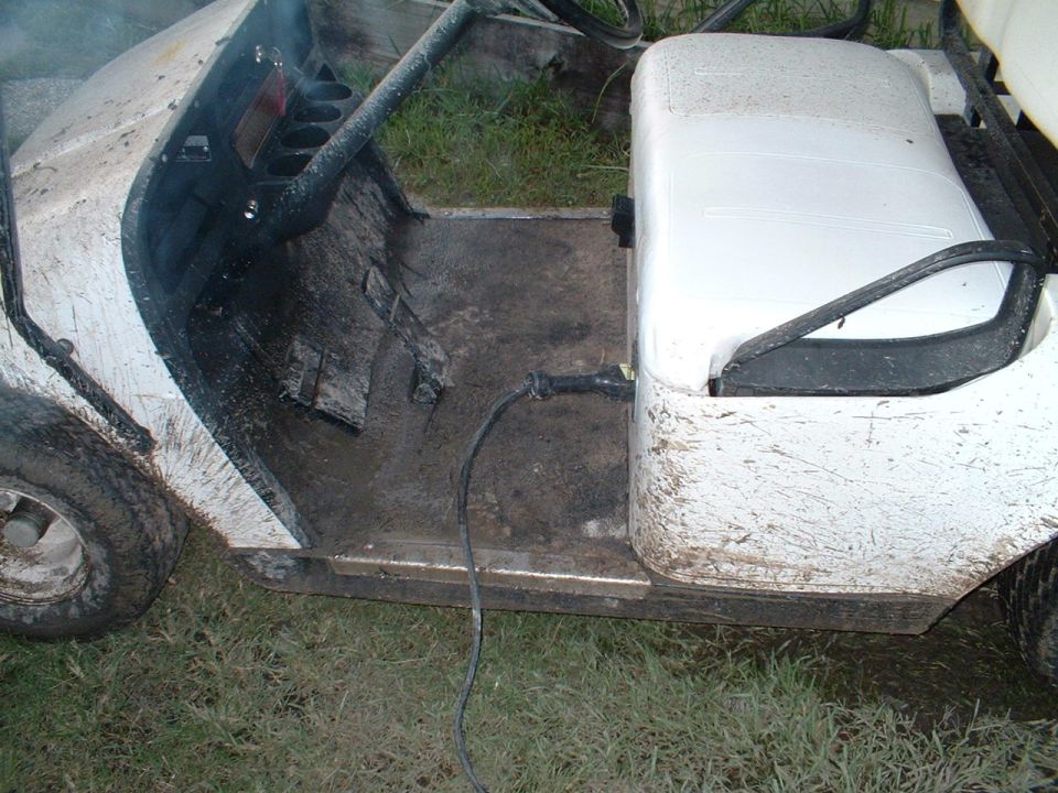 Mud-splattered white golf cart on grass with a cord across its floorboard