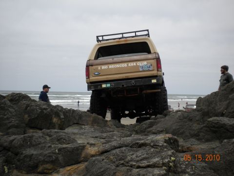 1994 Ford Explorer - A lifted Ford Bronco is parked on rocks near the ocean, with two people observing.
