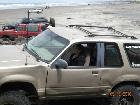 1994 Ford Explorer - A tan SUV with a woman driving is parked on a beach with other vehicles in the background.
