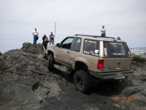 1994 Ford Explorer - Gold 2-door Ford Explorer with lifted suspension and off-road tires climbing over rocks near the ocean.