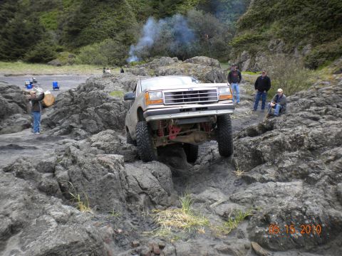 1994 Ford Explorer - A 1994 Ford Explorer tackles a challenging rocky path near the coast, with onlookers observing the off-road adventure.