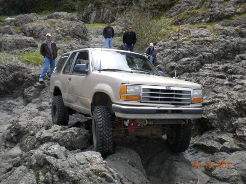 1994 Ford Explorer - A tan 1994 Ford Explorer navigates a rocky terrain, with several onlookers observing the off-road adventure.