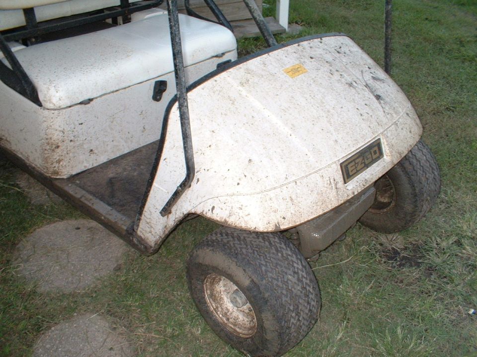 Mud-spattered white E-Z-GO golf cart parked on grass, front quarter view