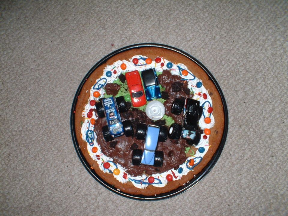 Cookie cake decorated with toy monster trucks and chocolate frosting mud pits