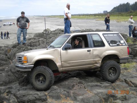 1994 Ford Explorer - A gold 1994 Ford Explorer is driven over rocks on a beach, with several people watching.