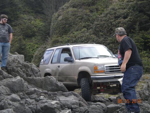 1994 Ford Explorer - A tan 1994 Ford Explorer is shown off-roading over a rocky coastal area.
