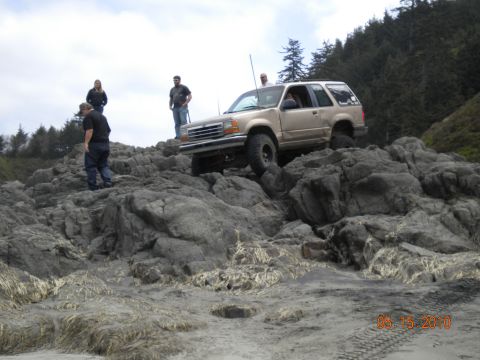 1994 Ford Explorer - A tan 1994 Ford Explorer navigates a rocky terrain, with several onlookers observing the off-road adventure.