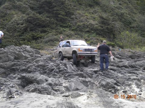 1994 Ford Explorer - A tan SUV with off-road modifications is driven over large rocks on a beach, with a date stamp of 05.15.2010.